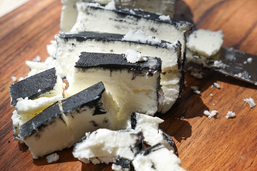Black ash dusted on sheep's milk cheese crumbling on a table. 