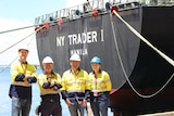 Four people wearing high-visibility shirts and hard hats standing in front of a cargo ship.