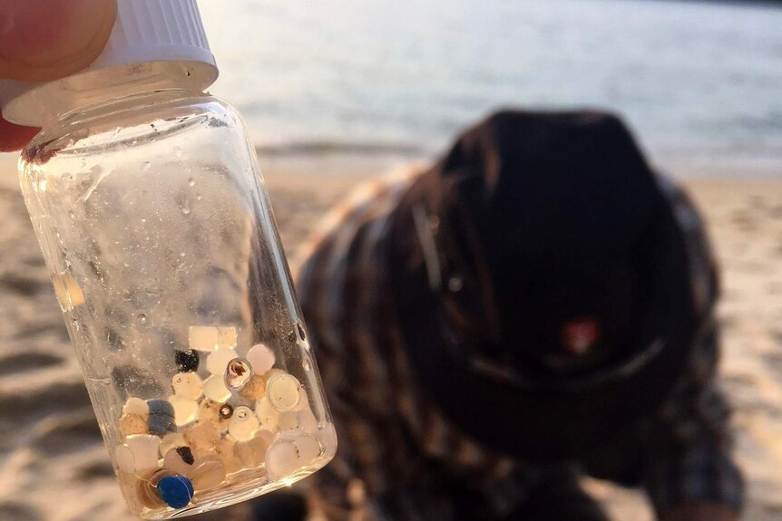 A tiny bottle with plastic fragments inside with a beach in the background.