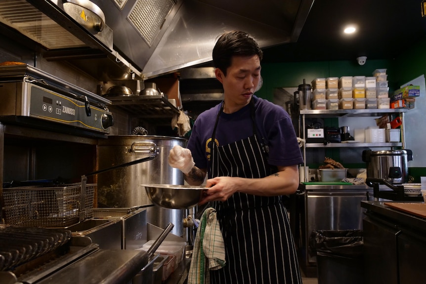 A chef holds a silver bowl with one hand covered in flour