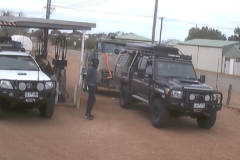 An indigenous man in front of two utes at a service station
