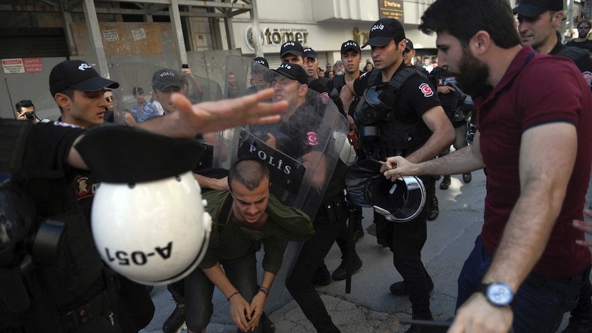 A group of riot police push a man with their shields.