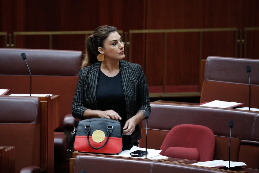 Thorpe stands on the senate floor with a handbag decorated with the Aboriginal flag resting in front of her.