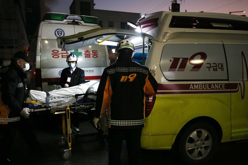 Paramedics wheel a body into an ambulance.