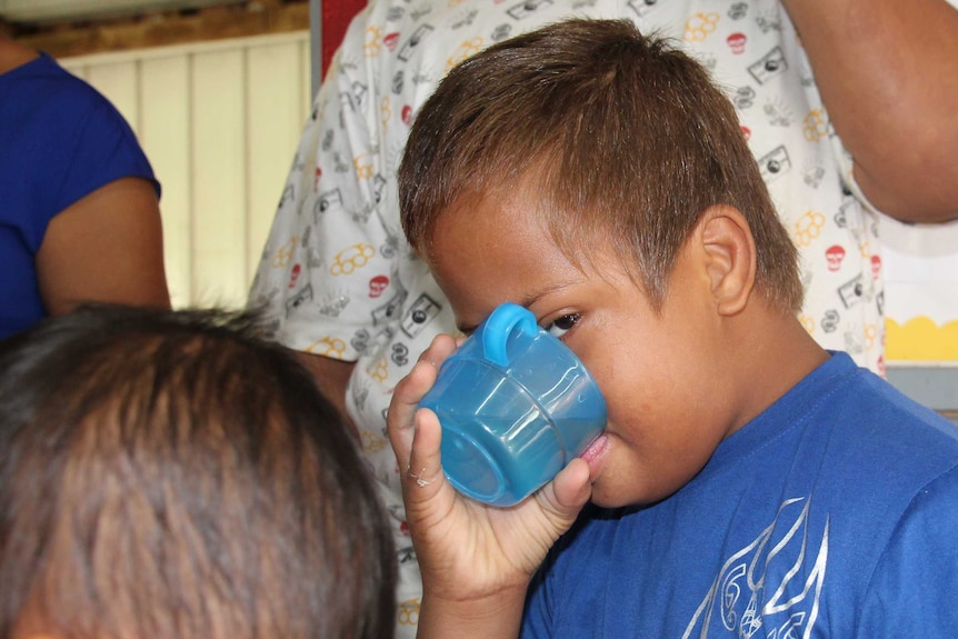 A boy drinks from a blue cup
