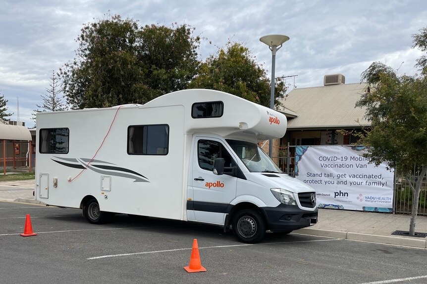 A side view of a white motorhome parked among orange cones next to a brown building.