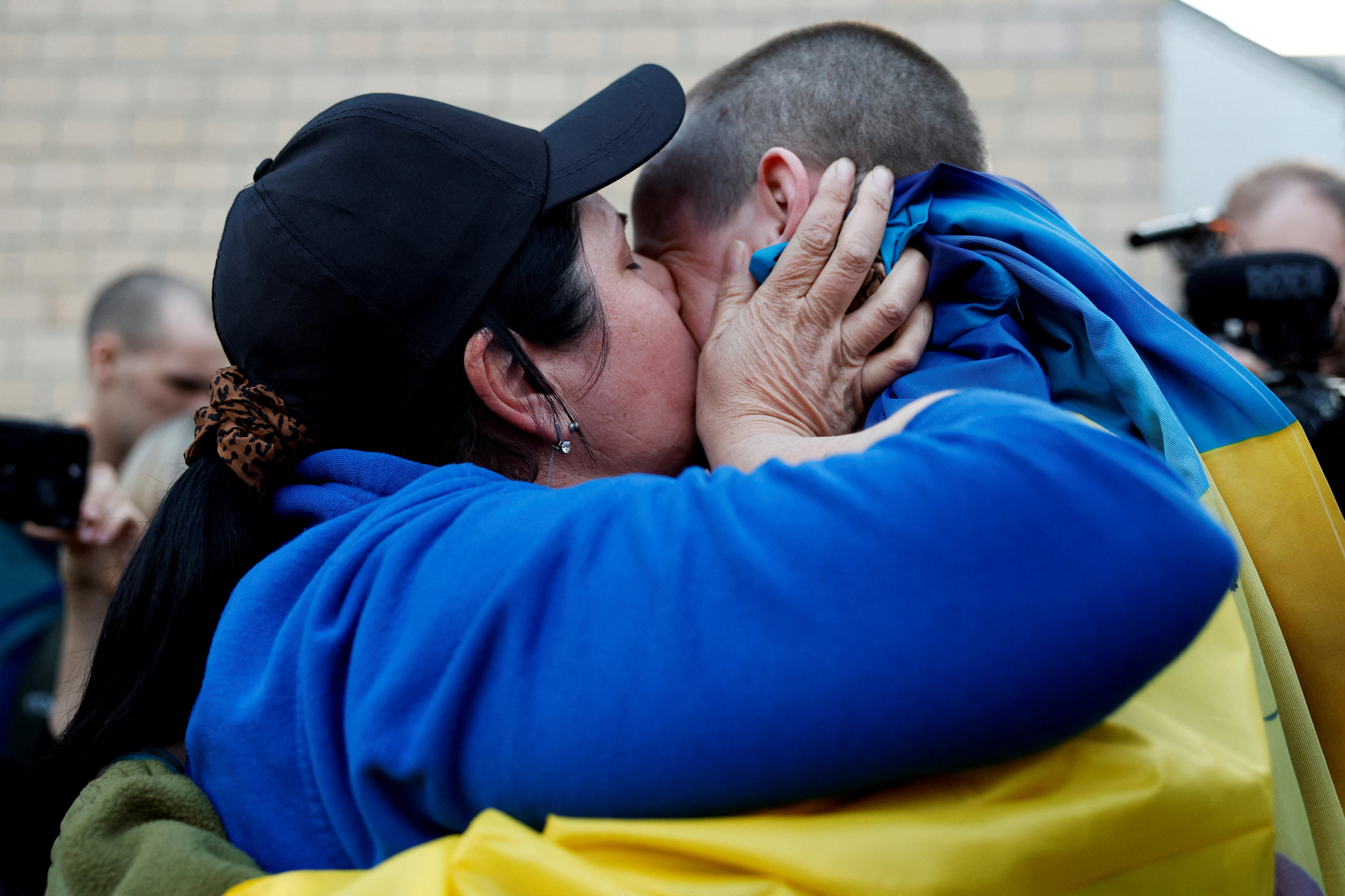 Woman embraces man wrapped in a Ukrainian flag and gives him a kiss on the cheek