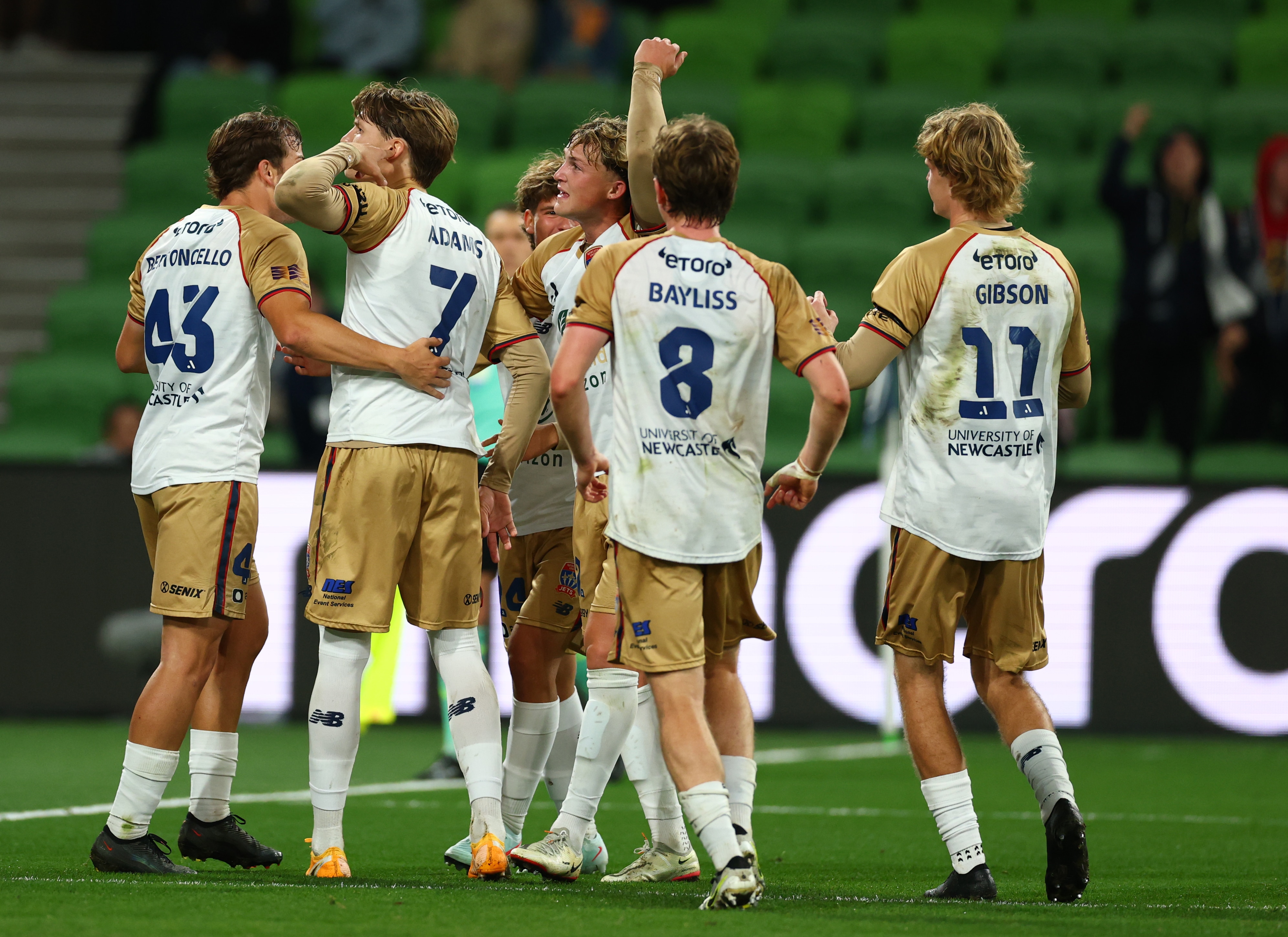 A group of soccer players in gold and white huddle and celebrate a goal
