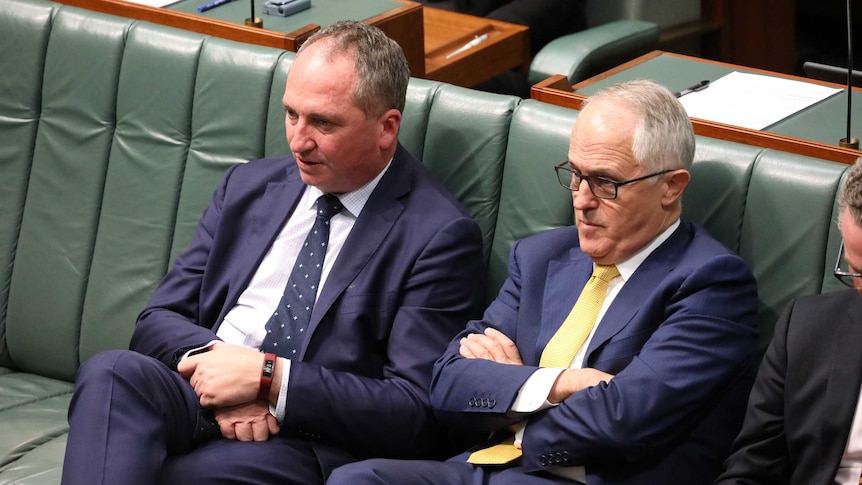 Barnaby Joyce, with his legs crossed and hands folded in his lap, next to Malcolm Turnbull, with arms folded across his chest.