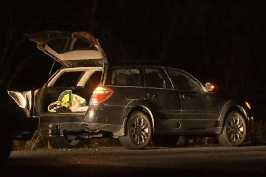 A car crashed by the side of the road at night.