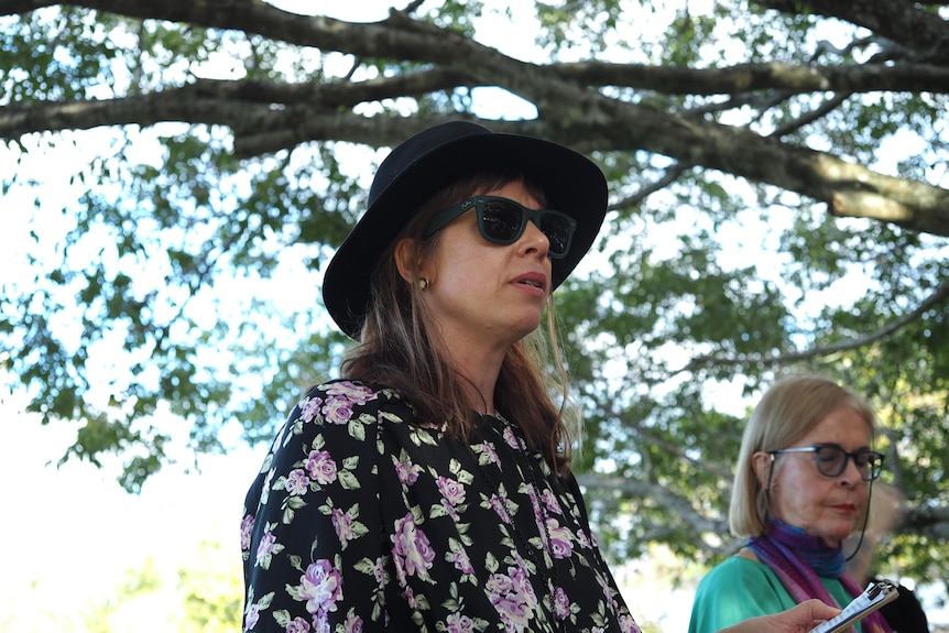 A woman in hat and glasses gives a speech