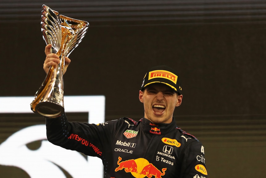 A man wearing a cap holds up an F1 trophy