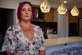 Tara stands in a floral dress in her kitchen.