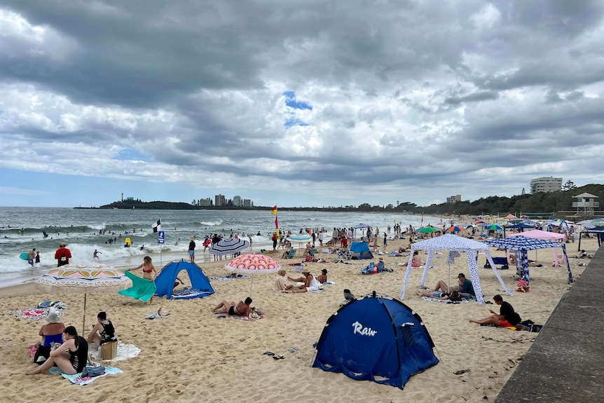 Busy beach with lots of cabanas and people in the water and stormy clouds above