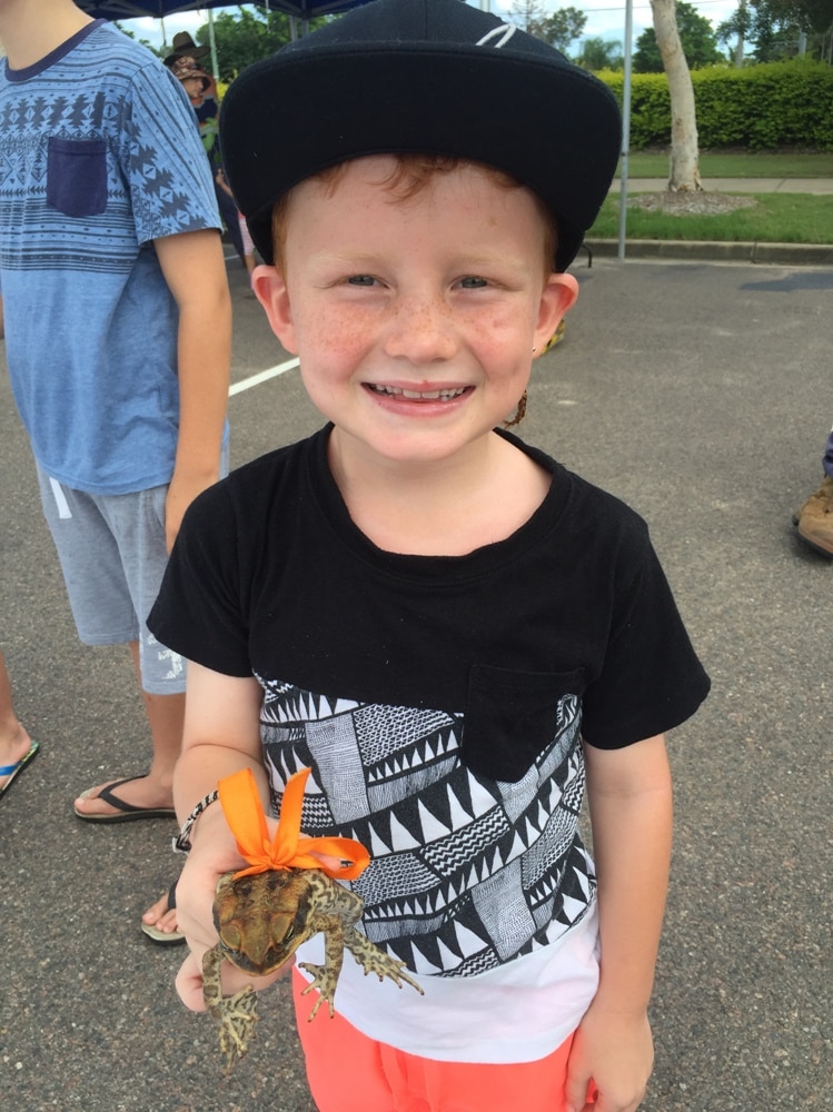 a boy holding a cane toad with an orange ribbon bow around it.