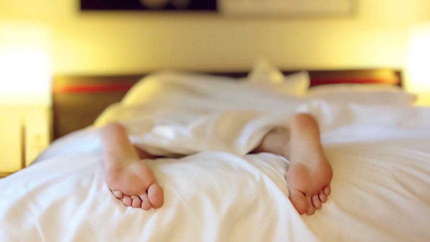 A person sleeps in a bed with white sheets, with their feet visible.