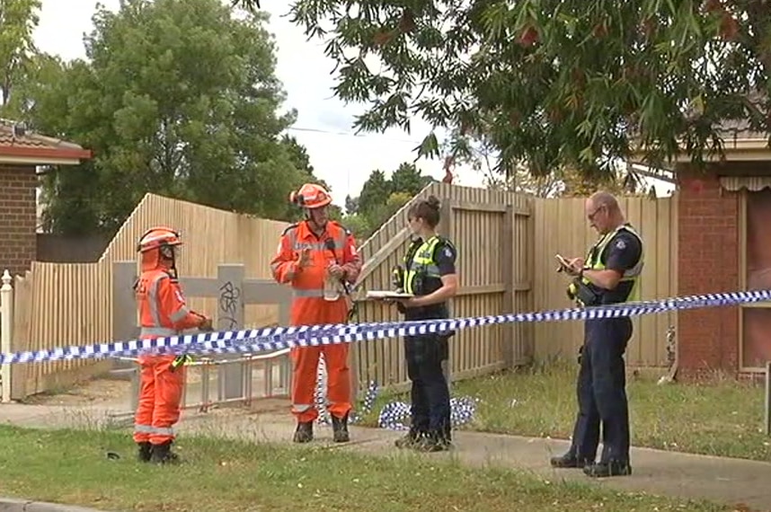 Police and emergency workers stand outside a brick house.