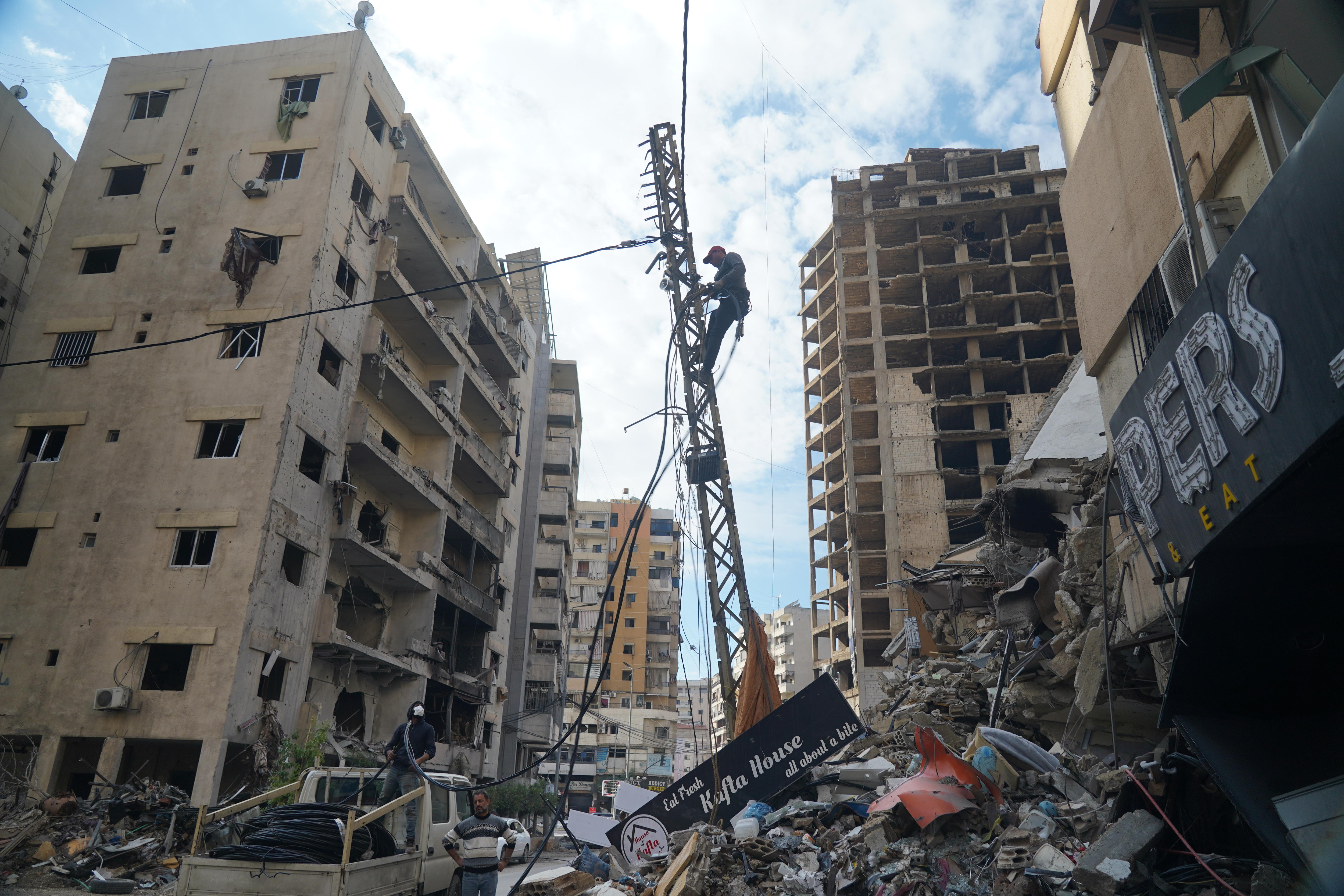 A photo of a man climbing up a crane, holding up a wire, with damaged buildings around him.