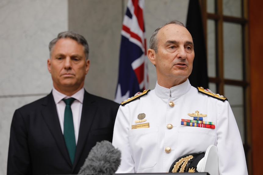 Marles and a man in navy uniform stand in a courtyard, an Australian flag behind them.