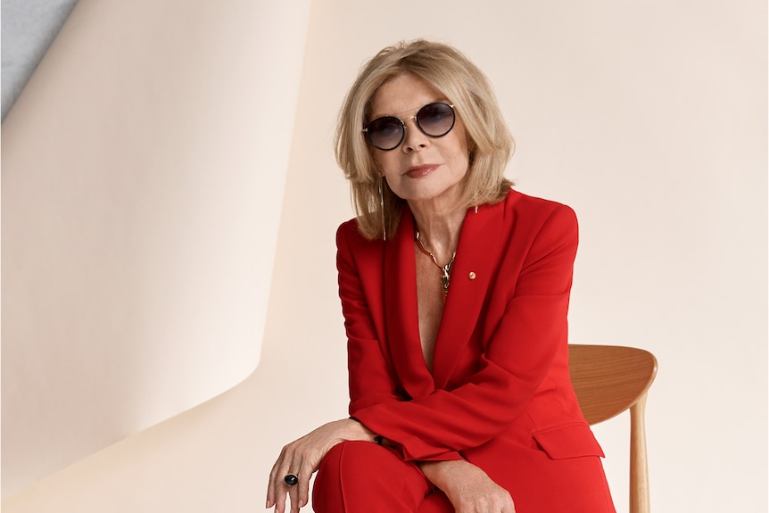 Fashion designer carla zampatti sits on chair dressed in red suit and sunglasses