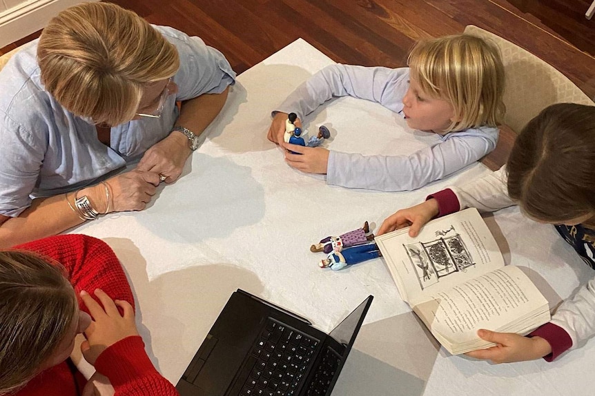 A woman sits at a table with three girls and a laptop.