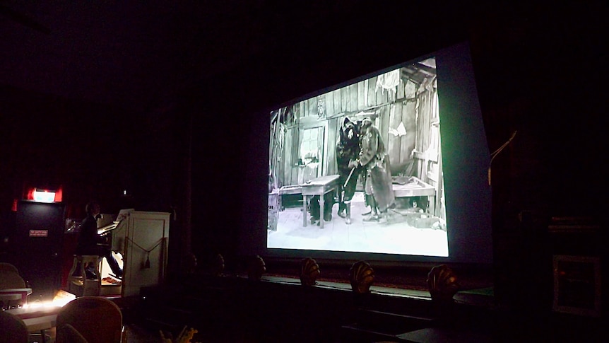 A pitch black theatre, with a film being projected onto it. 