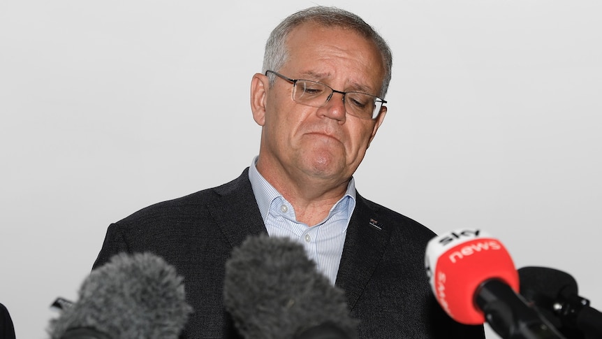 Scott Morrison stands at a lectern, frowning with this eyes closed.