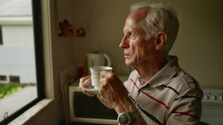 a man looking out the window holding a cup and saucer