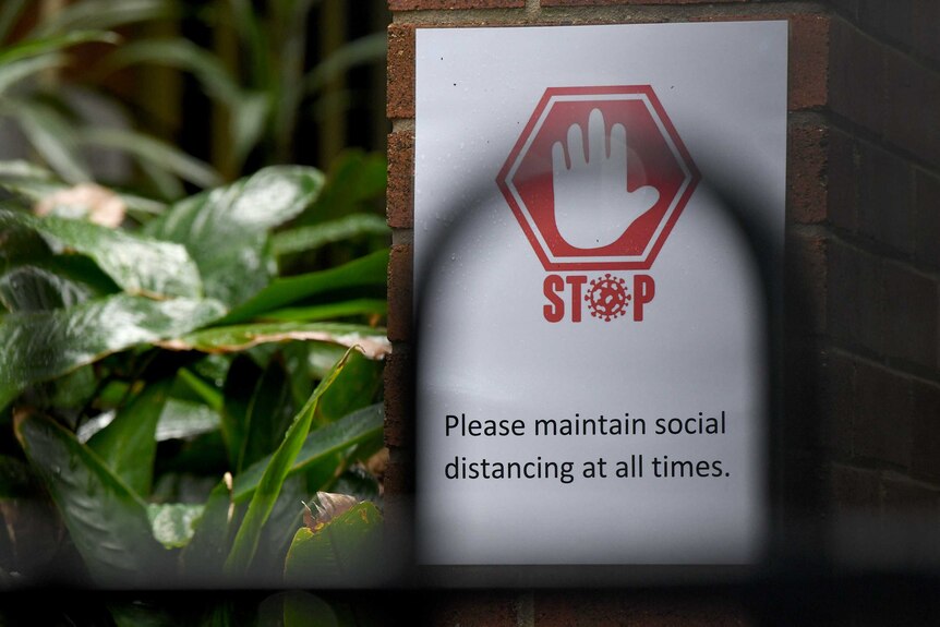 a social distancing sign near greenery at a school on a pillar