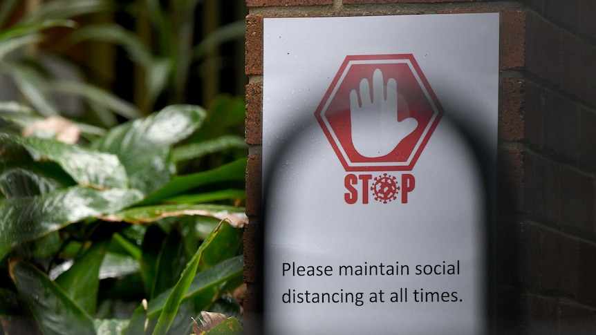 a social distancing sign near greenery at a school on a pillar