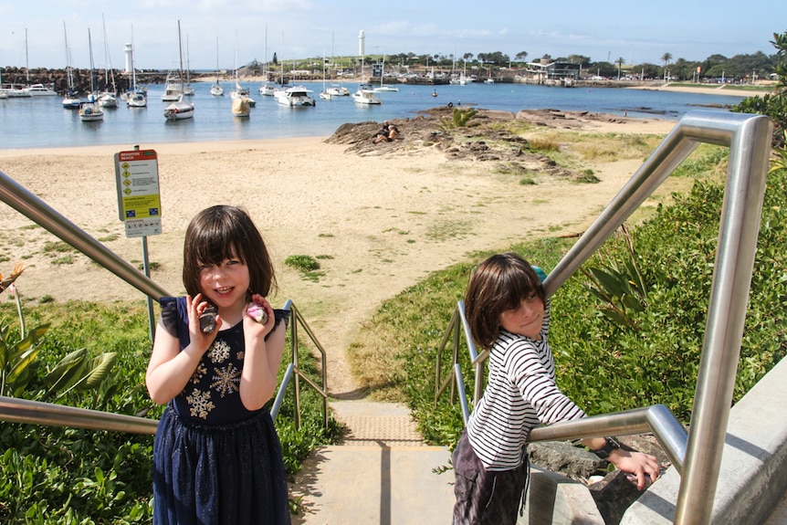 Two children stand on the steps leading to a harbour beach. 
