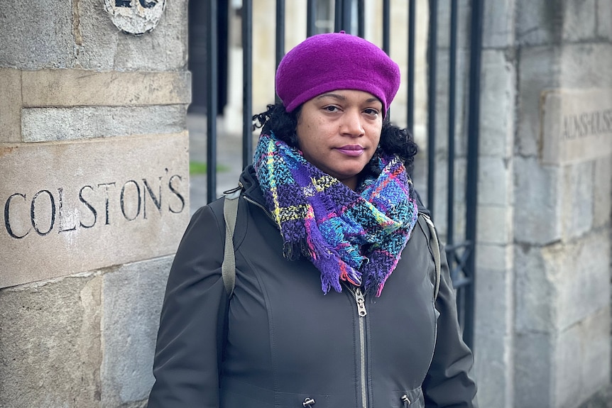 A black woman in a bright pink beret stands next to a sign reading 'Colston's'' 