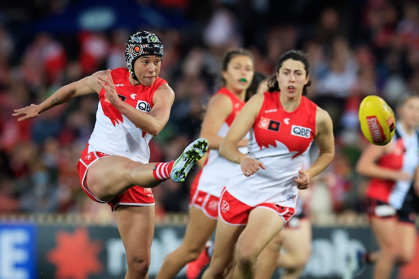 Aliesha Newman, wearing a helmet, kicks the ball away for the Sydney Swans