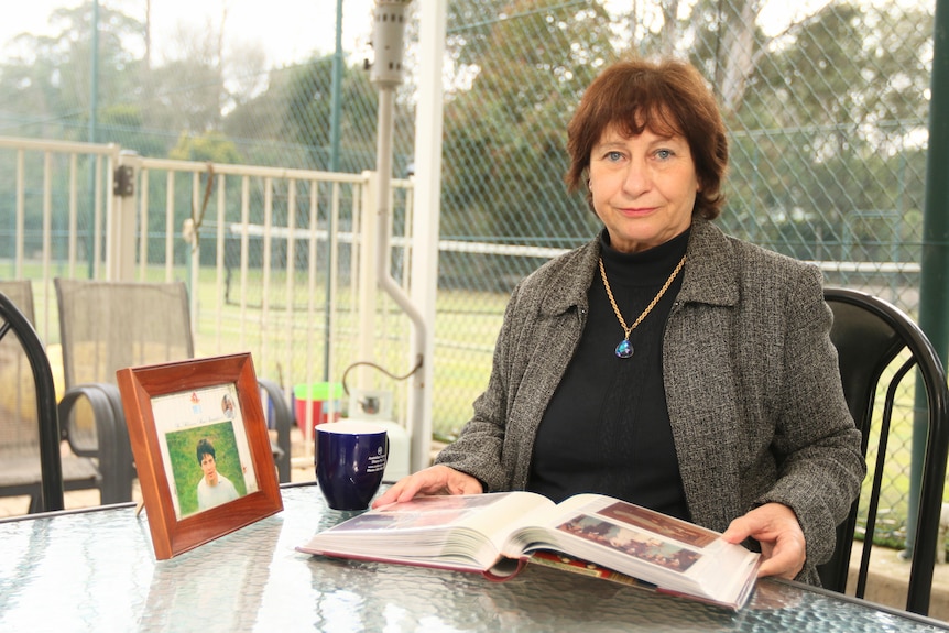 Carmen Martin sitting a table holding a family photo album, next to a framed photo of her brother.