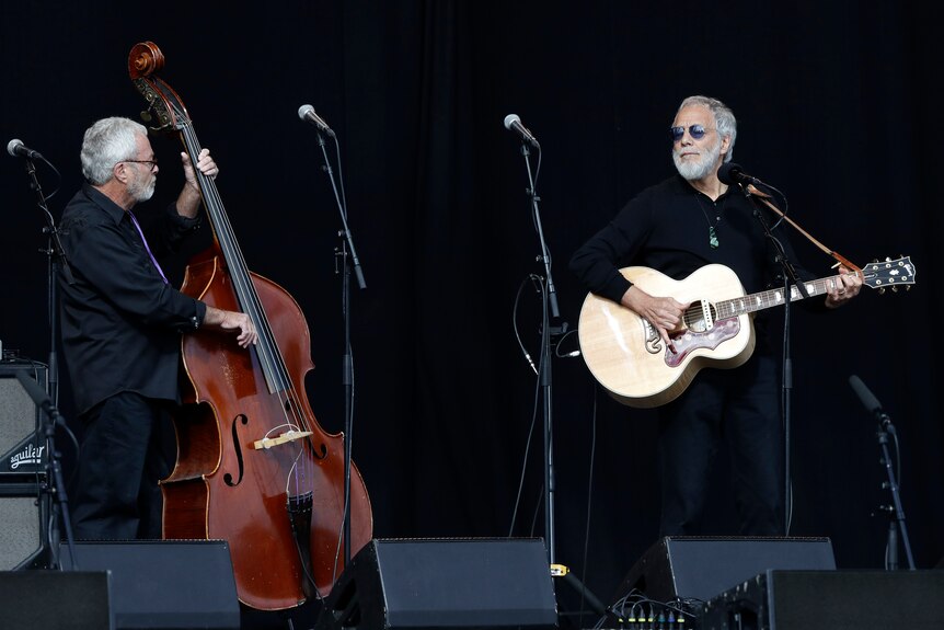 Cat Stevens plays guitar alongside a cello player on stage at a Christchurch remembrance service