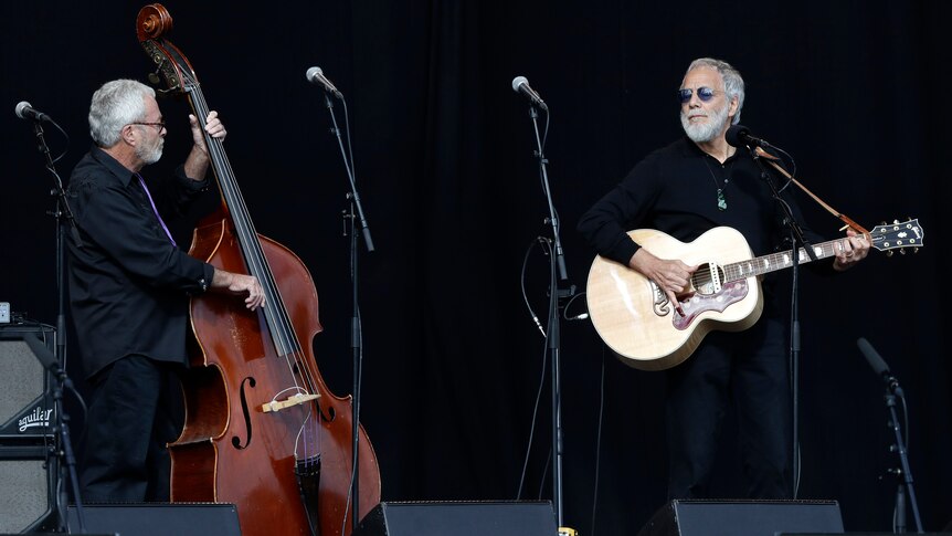 Cat Stevens plays guitar alongside a cello player on stage at a Christchurch remembrance service