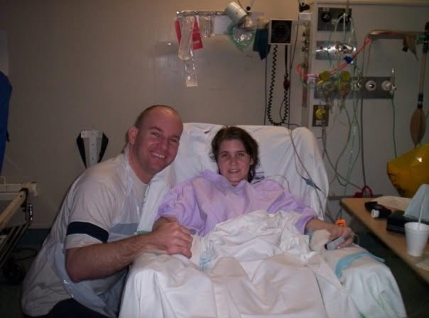 A woman in a hospital bed with a man by her side holding her hand, both are smiling.