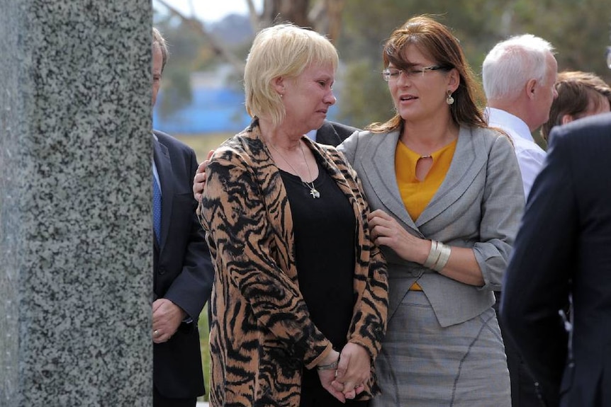 One woman puts her arm around the shoulder of a woman crying, at an outdoor memorial service