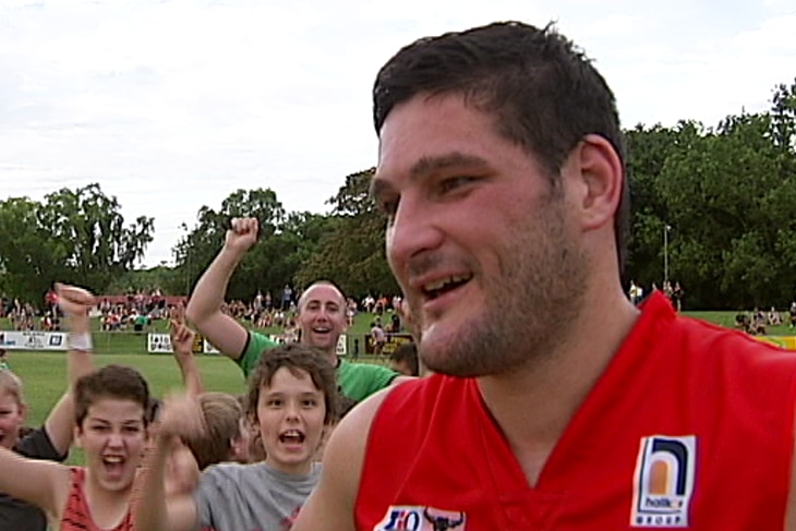 Close up of football player with kids celebrating behind him.