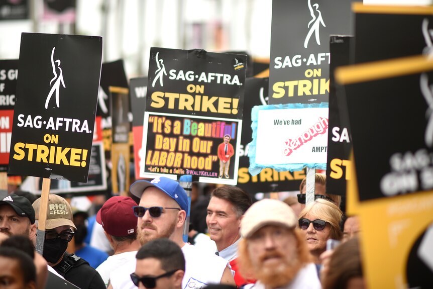Una multitud de manifestantes, algunos con sombreros y gafas de sol, sosteniendo carteles sobre la huelga de SAG-AFTRA.
