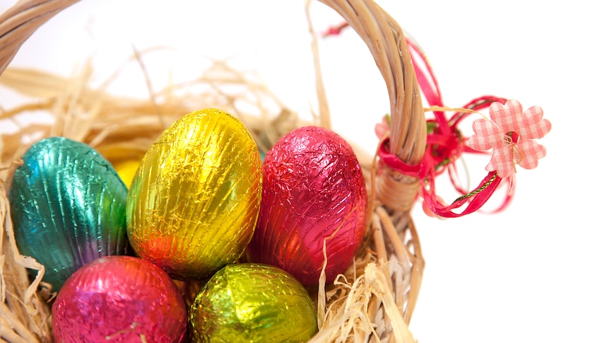 Multi-coloured foil-covered chocolate eggs in a straw basket