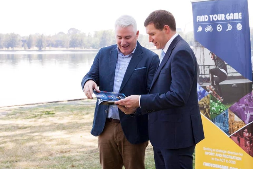 Two men in suits look at a pamphlet.