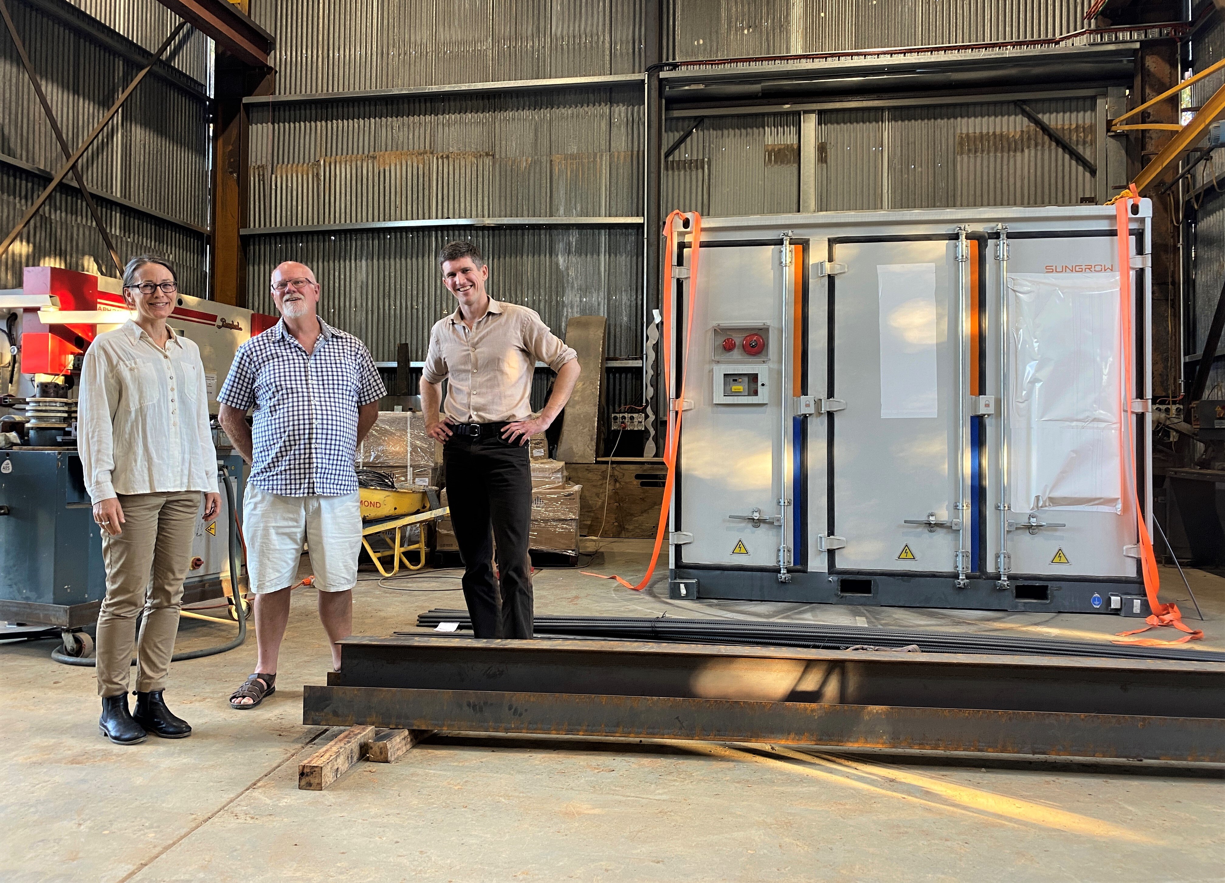 three people next to a big battery in a shed