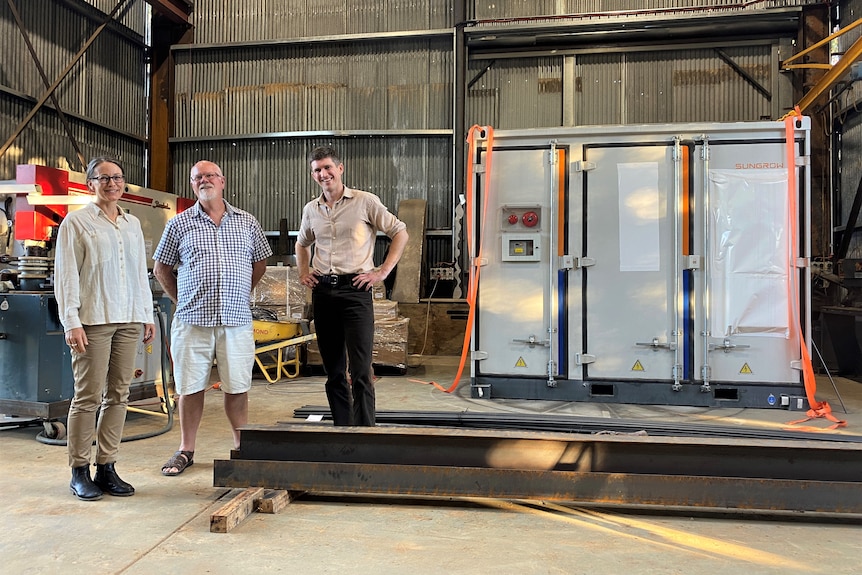 three people next to a big battery in a shed