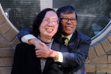 A Vietnamese Australian man smiles with his hands embracing his smiling wife. 