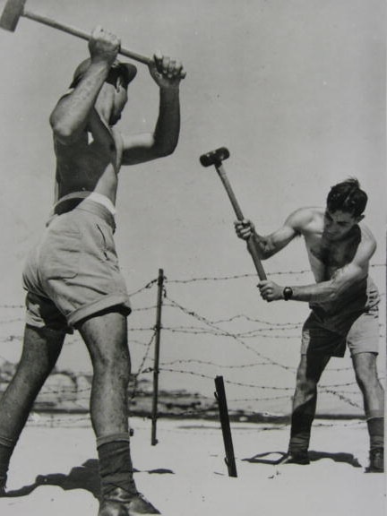 A black and white photo of two soldiers installing a barbed wire fence on Bondi Beach, 1942