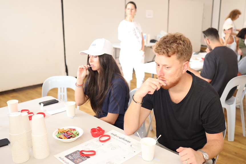 A young woman and a young man sitting at a table swabbing inside their cheeks