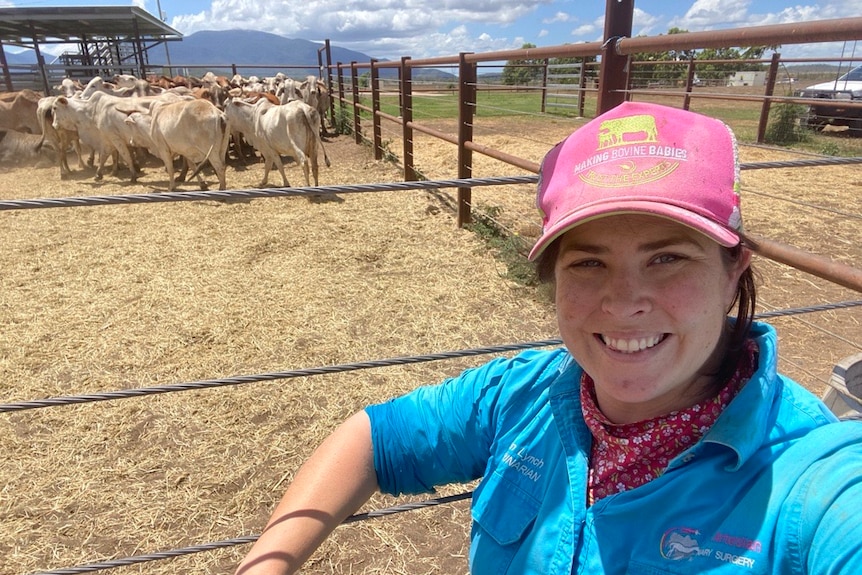 A smiling woman in a cap stands in front of a stockyard.