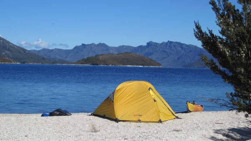 Picture of a yellow tent and kayak with water and mountains in the background.