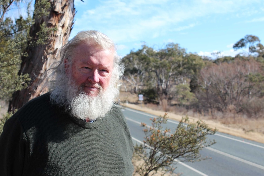 A man poses alongside a roadside in the bush.